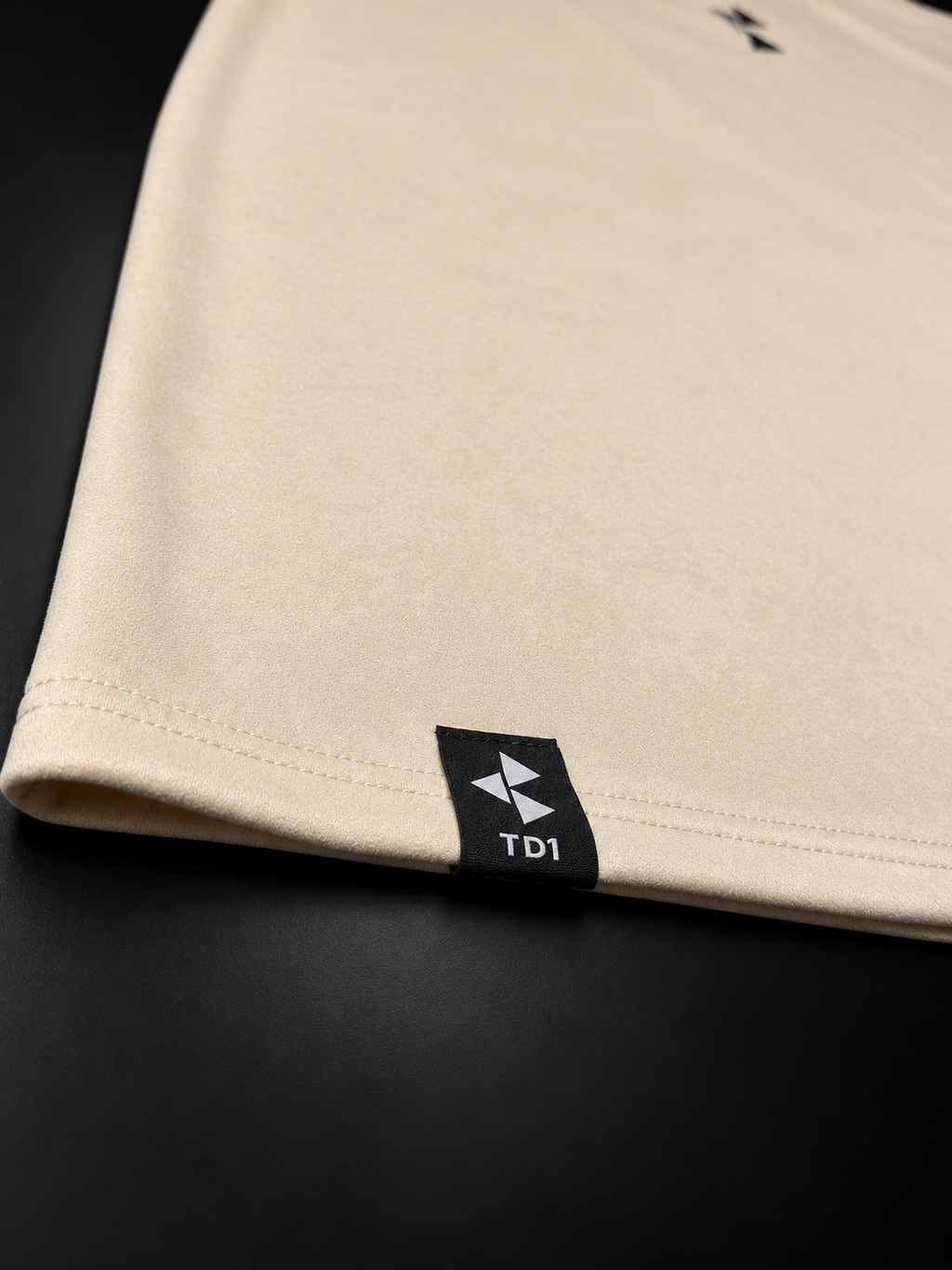TD1WORLD Engineered Winter Tee in Luxury Beige, close-up of stretch suede, stitched hem and woven TD1 label